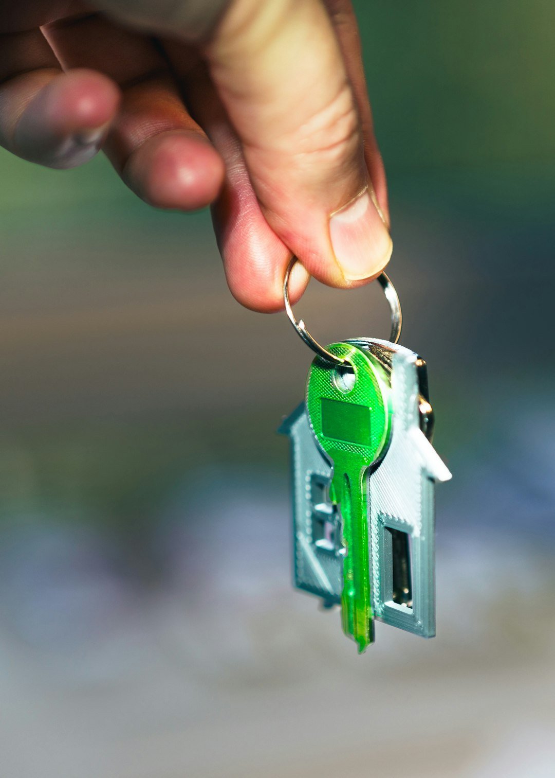 gallery-04 Hand holding green house key silver keychain outdoor setting during daylight real estate
