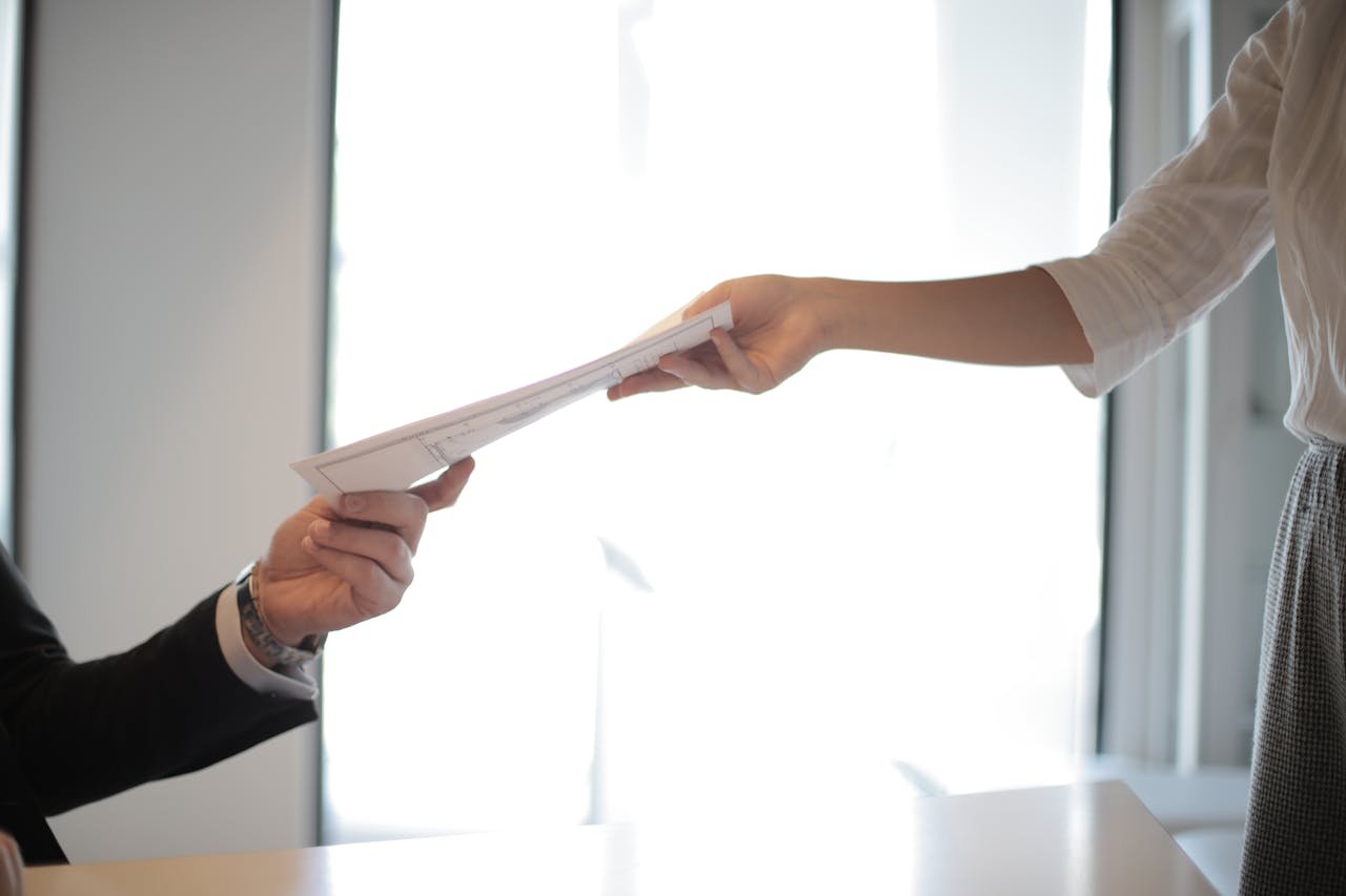 gallery-06 Close-up of hands exchanging documents in a business setting indoors.